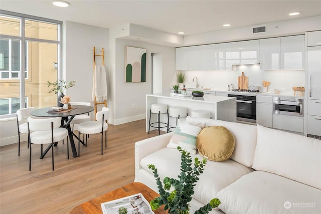 living area with visible vents, plenty of natural light, recessed lighting, light wood-style floors, and baseboards