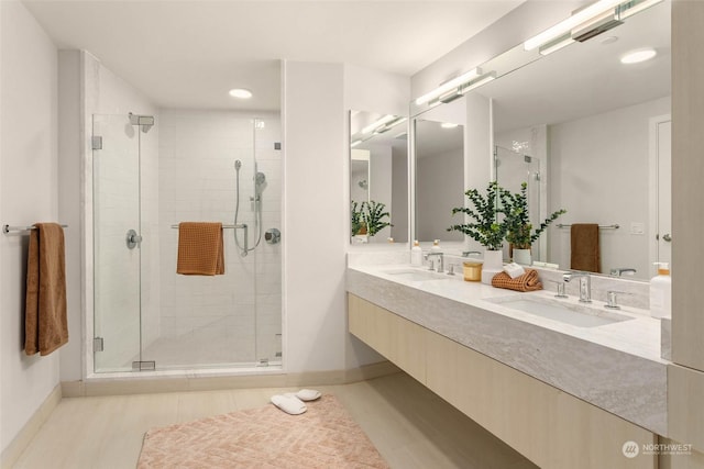 full bath with a sink, baseboards, a stall shower, and double vanity