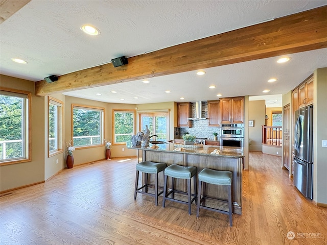 kitchen with dark stone countertops, a center island with sink, stainless steel appliances, and light hardwood / wood-style floors