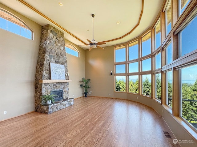 unfurnished living room featuring a fireplace, a tray ceiling, hardwood / wood-style flooring, ceiling fan, and a towering ceiling