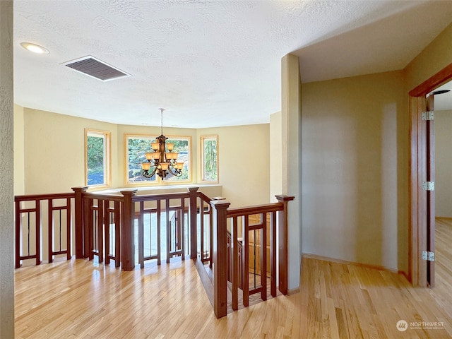 hallway featuring light wood-type flooring, a textured ceiling, and a notable chandelier