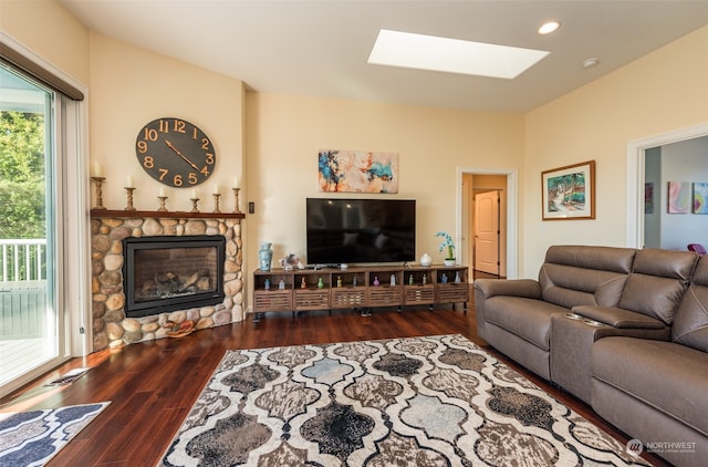 living room with a skylight, dark hardwood / wood-style floors, and a stone fireplace