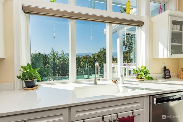 kitchen with white cabinets, light stone counters, stainless steel dishwasher, and sink