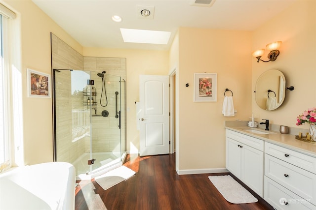 bathroom featuring a skylight, wood finished floors, vanity, baseboards, and a shower stall