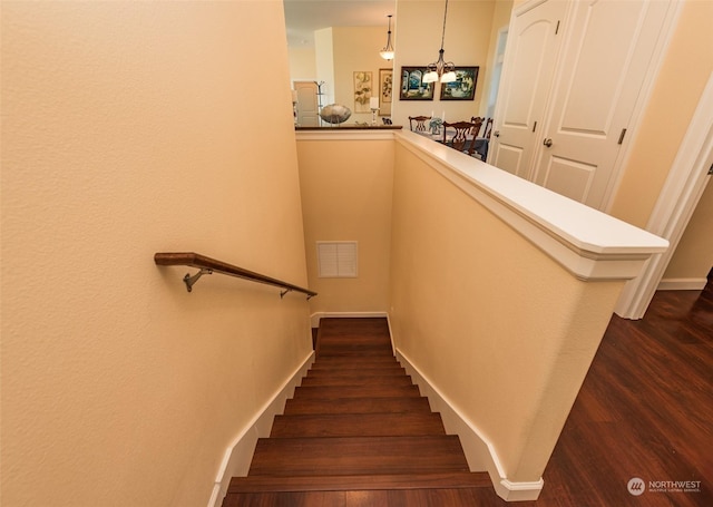 stairway featuring an inviting chandelier, wood finished floors, visible vents, and baseboards