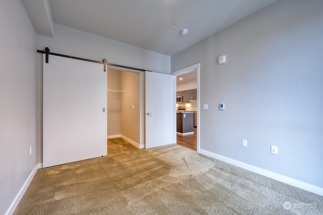 unfurnished bedroom featuring a barn door, a closet, light colored carpet, and a spacious closet