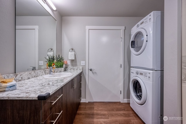 clothes washing area featuring stacked washing maching and dryer, dark hardwood / wood-style flooring, and sink