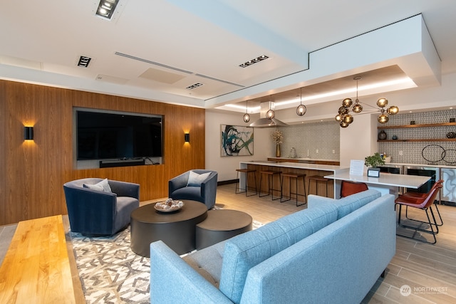 living room featuring a raised ceiling, an inviting chandelier, and light wood-type flooring