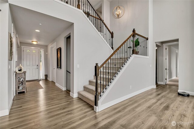 entrance foyer with a towering ceiling, a chandelier, and light wood-type flooring