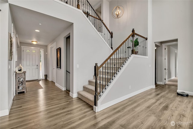 foyer entrance featuring stairs, light wood finished floors, an inviting chandelier, and baseboards