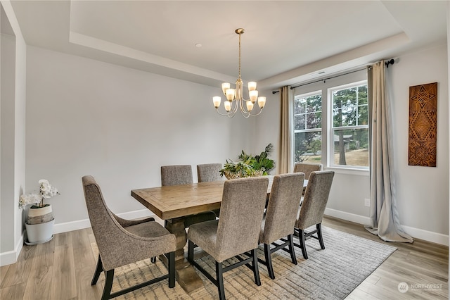 dining area featuring a raised ceiling, light hardwood / wood-style flooring, and a notable chandelier