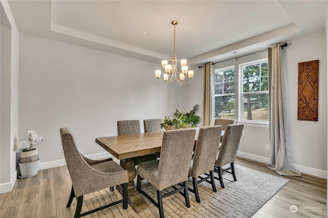 dining area with light wood-type flooring, baseboards, a raised ceiling, and a notable chandelier