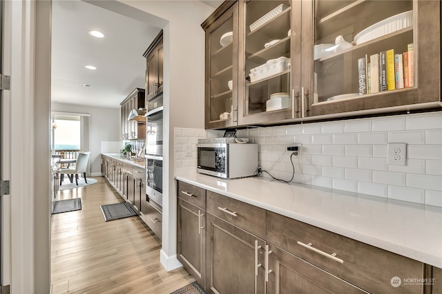 kitchen with backsplash, dark brown cabinetry, stainless steel appliances, and light hardwood / wood-style floors