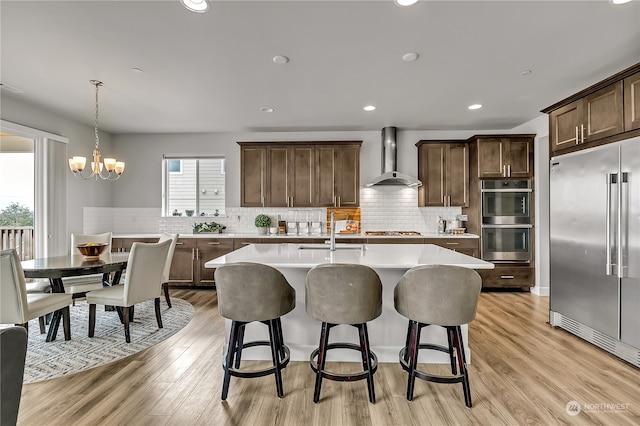 kitchen with stainless steel appliances, sink, wall chimney range hood, pendant lighting, and light hardwood / wood-style floors