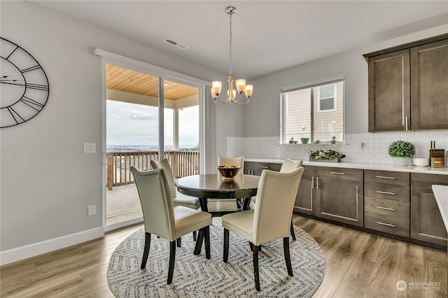 dining area with light wood-type flooring, a healthy amount of sunlight, and a notable chandelier