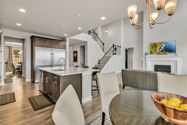 kitchen featuring a center island with sink, sink, light hardwood / wood-style flooring, stainless steel dishwasher, and dark brown cabinets