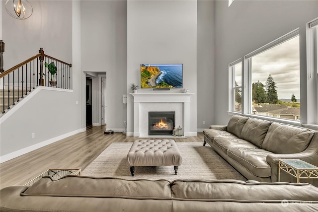 living area featuring baseboards, a glass covered fireplace, stairway, wood finished floors, and a notable chandelier