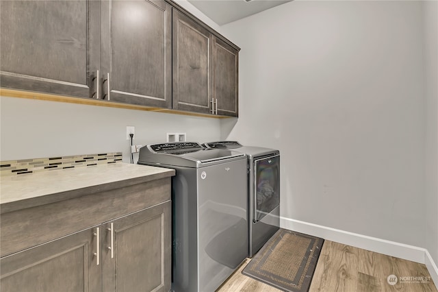 laundry room with washer and clothes dryer, light hardwood / wood-style flooring, and cabinets