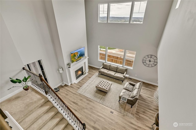 living area with stairs, a high ceiling, wood finished floors, and a glass covered fireplace