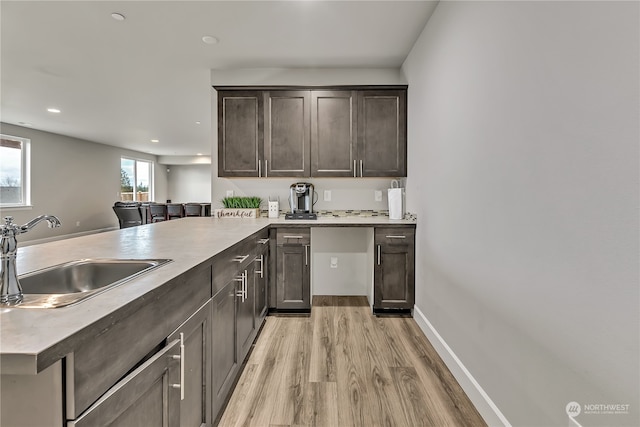 kitchen with light wood-style floors, a sink, dark brown cabinetry, a peninsula, and baseboards