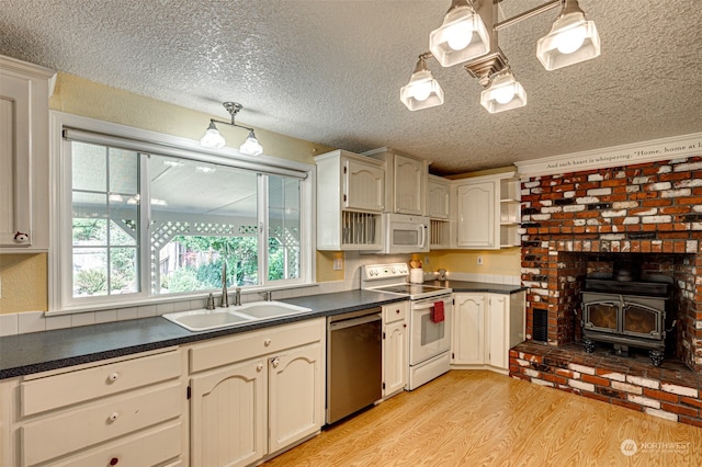 kitchen featuring light hardwood / wood-style floors, a wood stove, a textured ceiling, sink, and white appliances