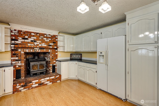 kitchen with a wood stove, light hardwood / wood-style floors, white cabinets, and white refrigerator with ice dispenser