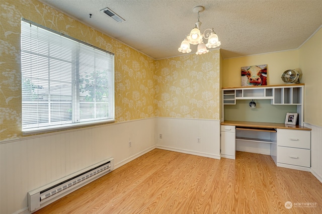 unfurnished office featuring a wealth of natural light, light hardwood / wood-style floors, built in desk, and a baseboard heating unit