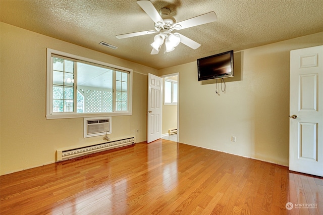 empty room featuring a wall unit AC, light wood-type flooring, a baseboard radiator, and ceiling fan