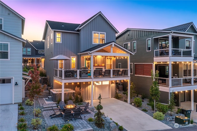 back house at dusk with a balcony, a fire pit, a patio area, and central AC