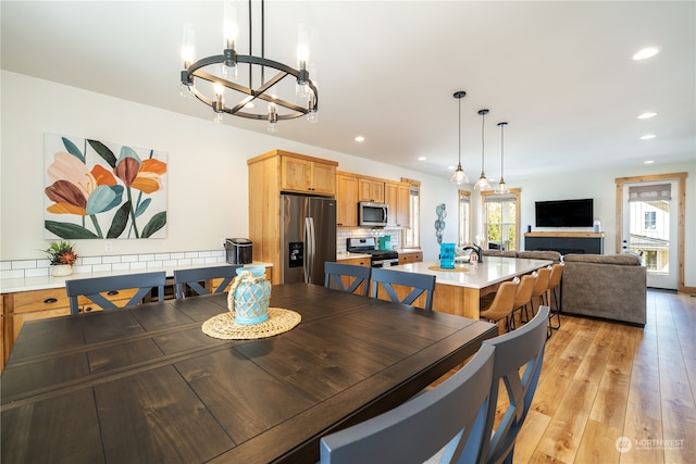 dining room with light wood-type flooring, a tiled fireplace, and an inviting chandelier