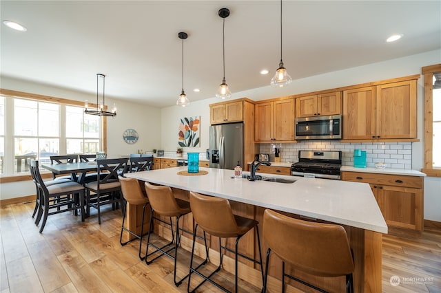 kitchen with decorative light fixtures, appliances with stainless steel finishes, light hardwood / wood-style floors, and sink