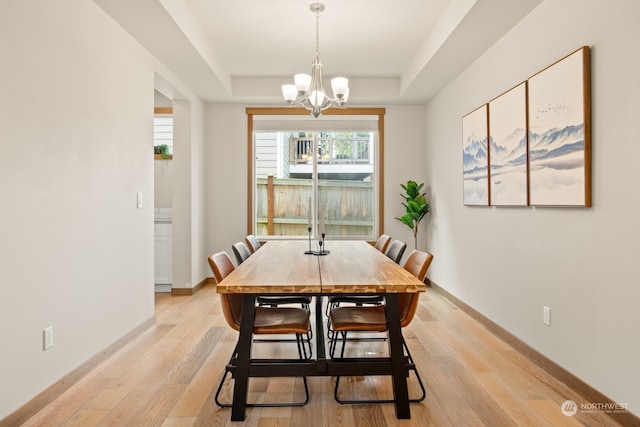 dining room with a chandelier, a raised ceiling, and light hardwood / wood-style flooring