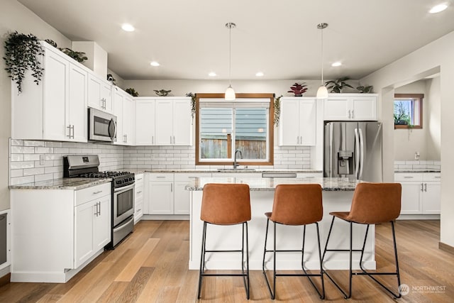 kitchen with white cabinets, light hardwood / wood-style flooring, appliances with stainless steel finishes, light stone countertops, and pendant lighting