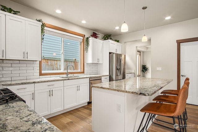 kitchen featuring appliances with stainless steel finishes, white cabinetry, a kitchen island, and sink