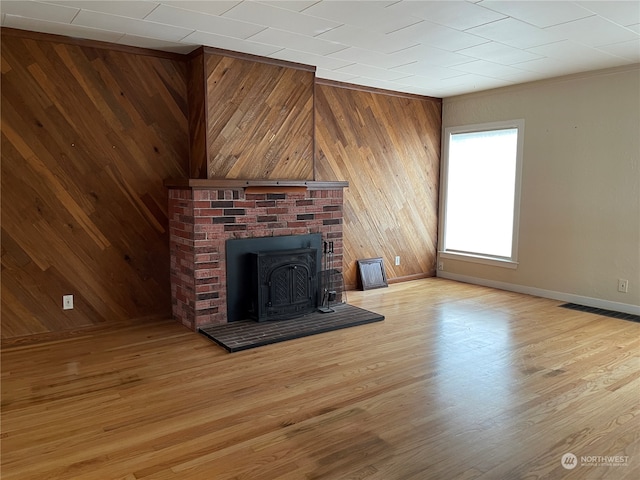 unfurnished living room with a wood stove, wooden walls, light hardwood / wood-style floors, and ornamental molding