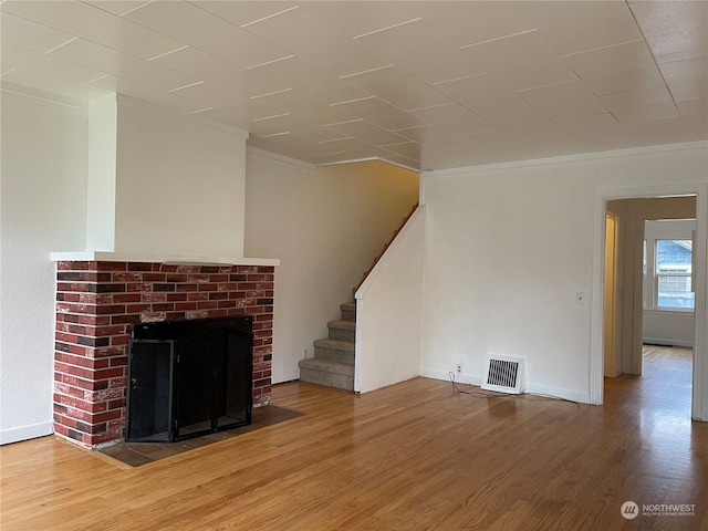 unfurnished living room featuring ornamental molding, a brick fireplace, and hardwood / wood-style flooring