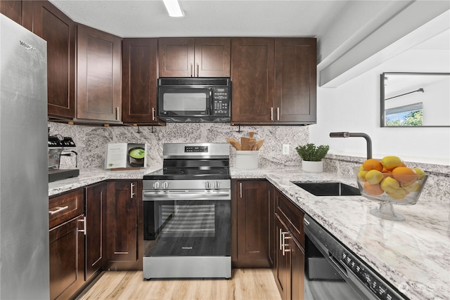 kitchen with light hardwood / wood-style flooring, black appliances, sink, light stone countertops, and decorative backsplash