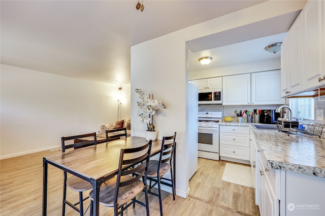 kitchen with white appliances, sink, decorative backsplash, white cabinetry, and light wood-type flooring