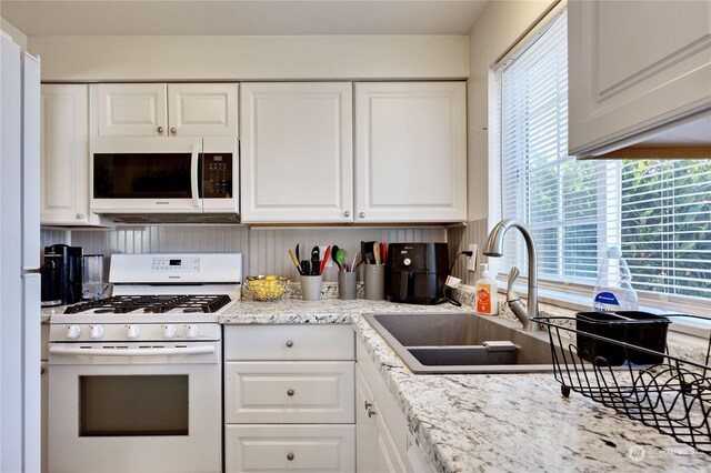 kitchen featuring white cabinetry, white appliances, plenty of natural light, and light stone counters