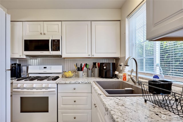 kitchen with white appliances, white cabinetry, and a sink