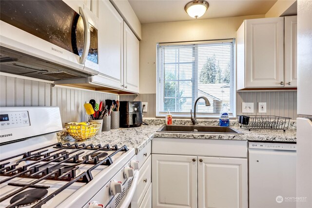 kitchen with white cabinetry, white appliances, light stone counters, and sink