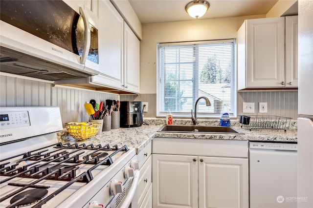 kitchen with white appliances, white cabinets, a sink, and light stone countertops