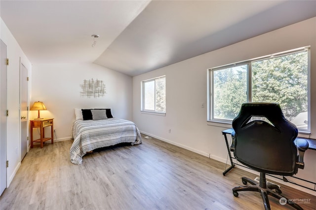 bedroom with vaulted ceiling, baseboards, and light wood-style floors