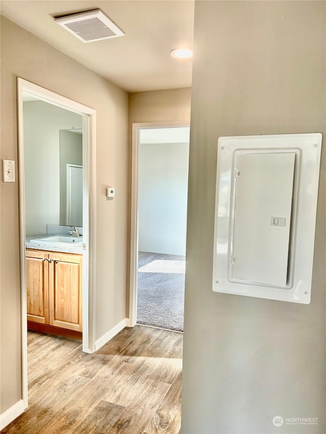 hall featuring electric panel, light hardwood / wood-style flooring, and sink