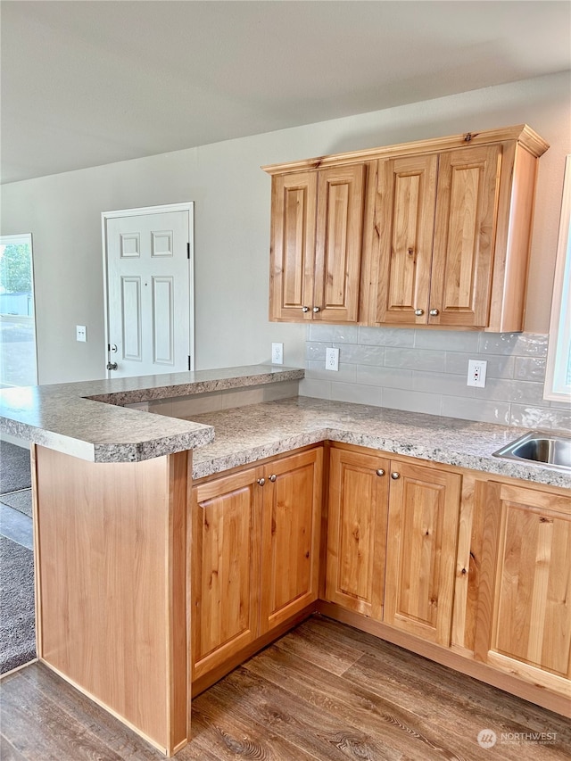 kitchen with kitchen peninsula, sink, hardwood / wood-style floors, and tasteful backsplash