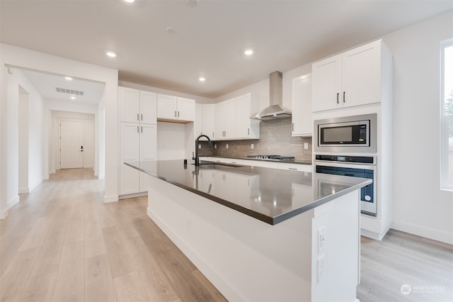 kitchen with stainless steel appliances, dark countertops, visible vents, a sink, and wall chimney range hood