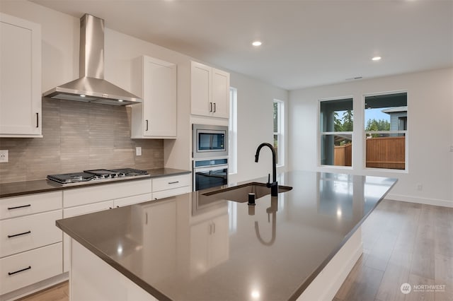 kitchen featuring dark countertops, wall chimney range hood, stainless steel appliances, and a sink