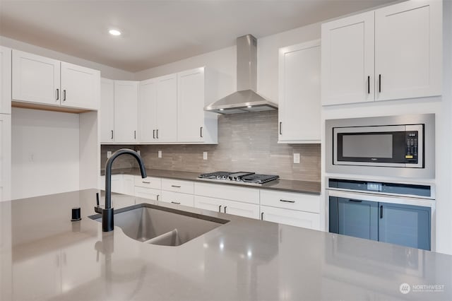 kitchen featuring dark countertops, appliances with stainless steel finishes, white cabinets, a sink, and wall chimney exhaust hood