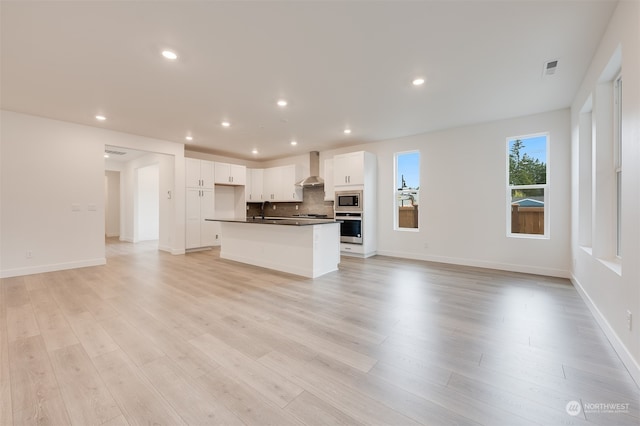 kitchen with dark countertops, wall chimney exhaust hood, appliances with stainless steel finishes, open floor plan, and backsplash