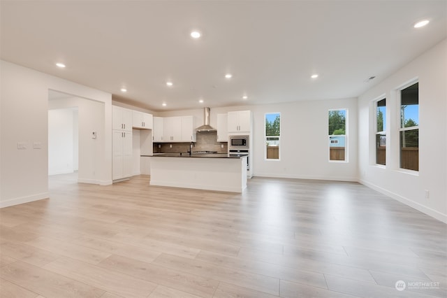 kitchen with dark countertops, decorative backsplash, appliances with stainless steel finishes, open floor plan, and wall chimney range hood